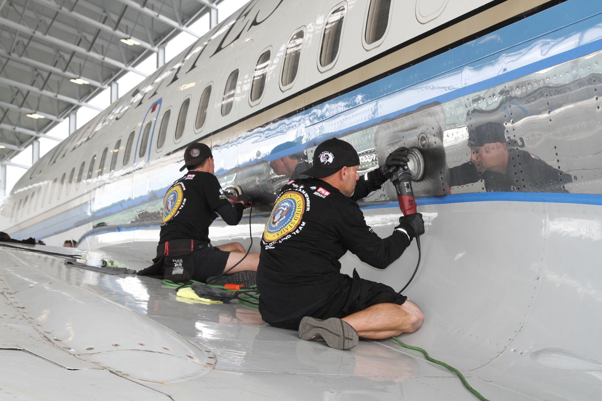 Two people polishing the side of an airplane in a hangar. Shiny metal reflects their faces.