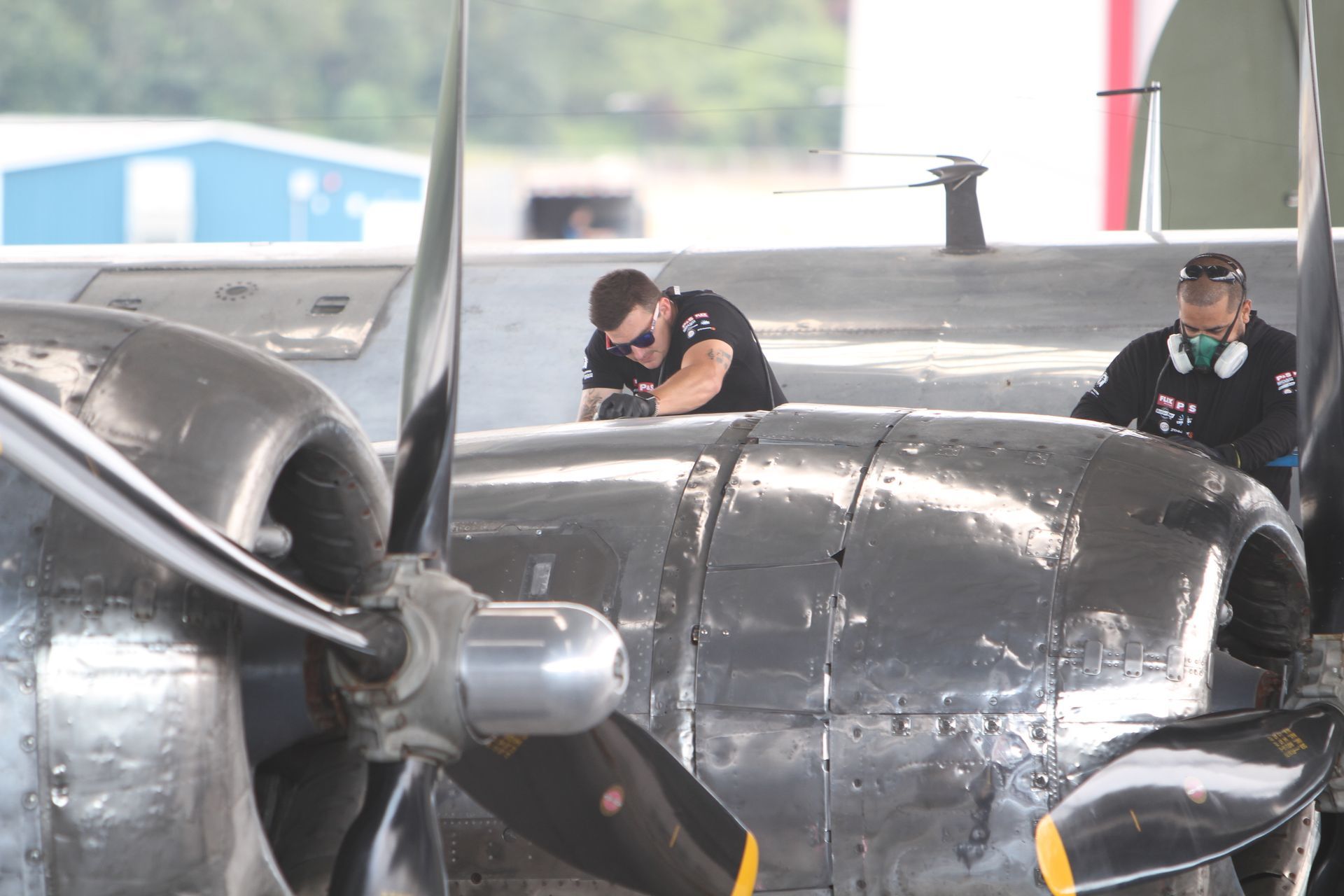 Two mechanics working on the engine of a vintage aircraft, outdoors.