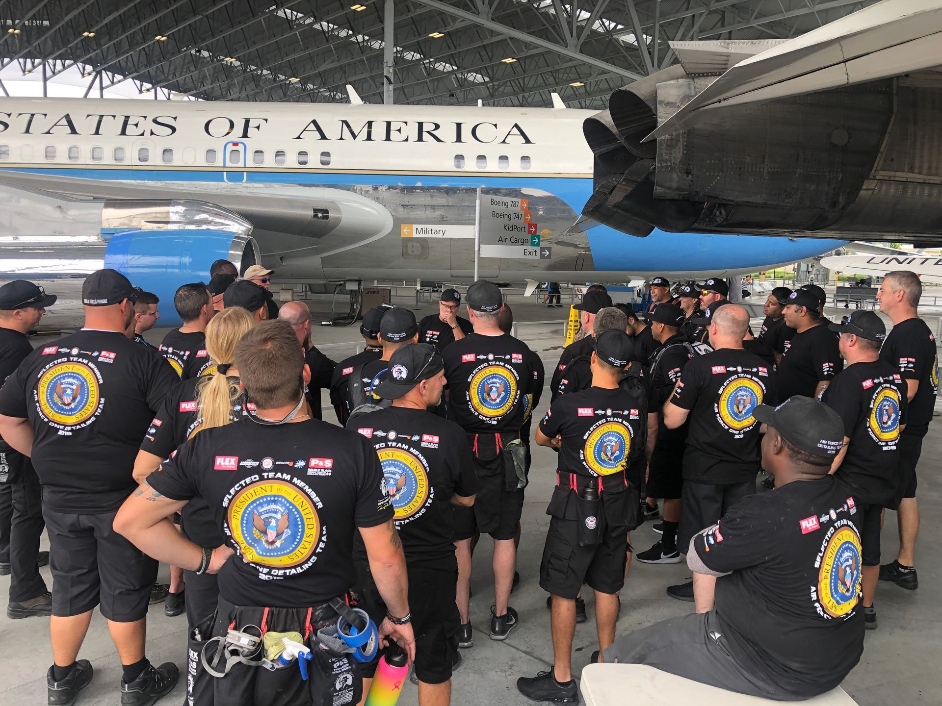 Group of people in black shirts with a logo, standing near an airplane labeled 