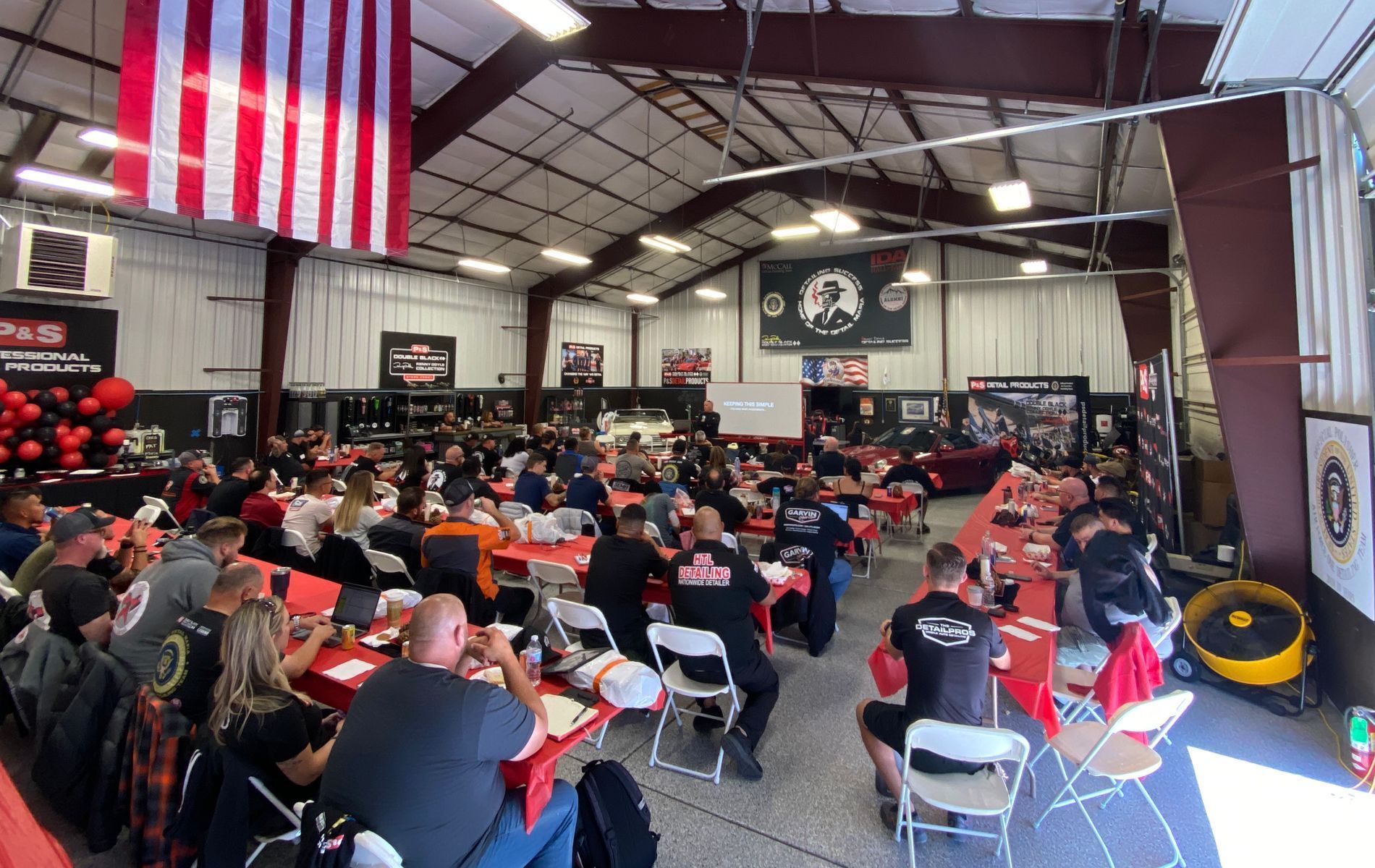 Large gathering in a garage, people at tables, American flag hanging, red decorations.
