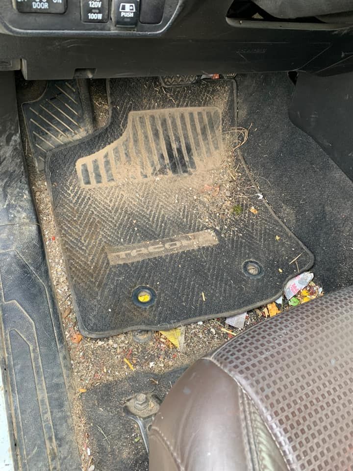 Dirty black car floor mat in a vehicle interior with debris.