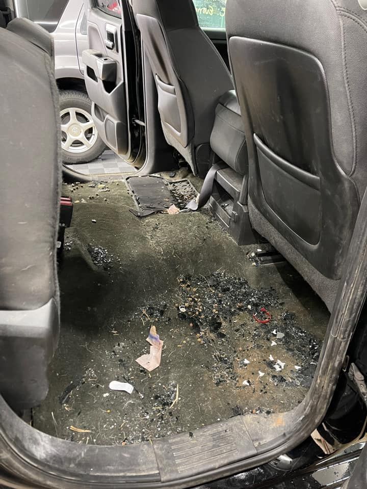 Dirty black car interior. Debris covers the floor; seats are visible.