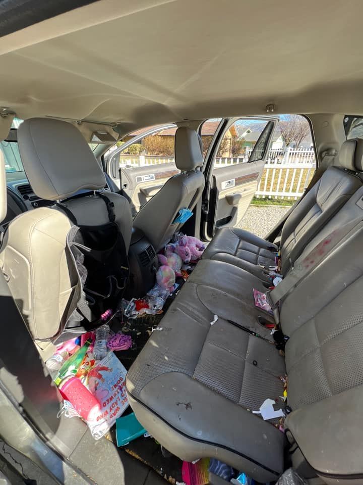 Interior of a car in disarray; trash and belongings are strewn across the seats and floor.