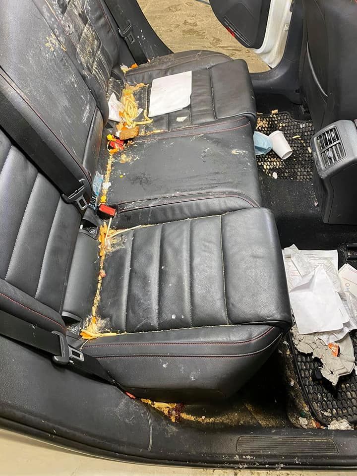 Dirty car back seat with food and trash strewn across the black leather.