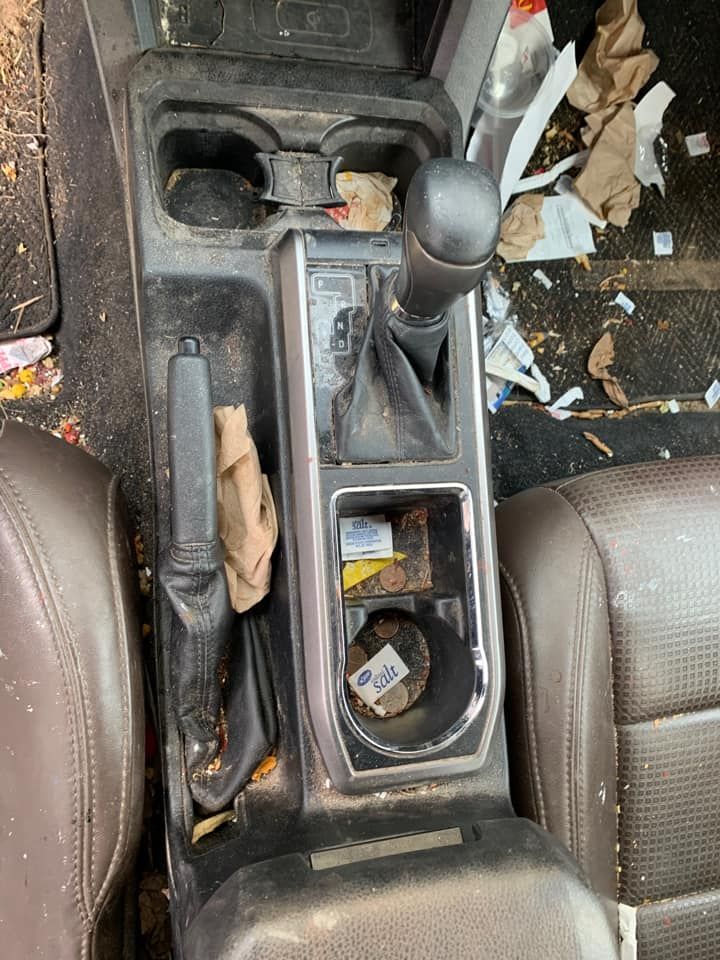 Dirty car interior with a gear shift, cup holders, and trash. Brown seats.