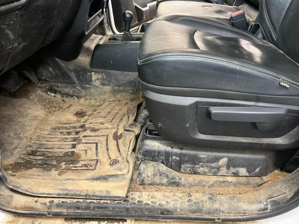 Dirty vehicle interior; mud-covered floor mat, black leather seat, and visible gear shift.