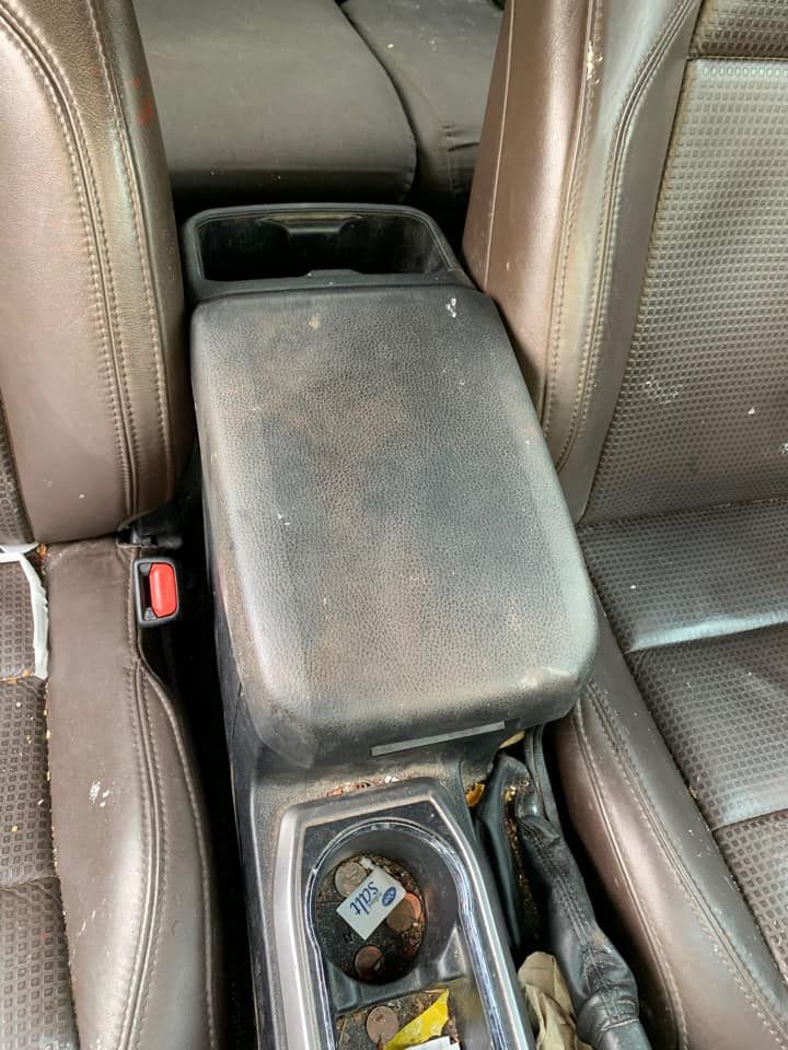Center console of a car, brown leather seats. The console lid and surrounding area are dirty.