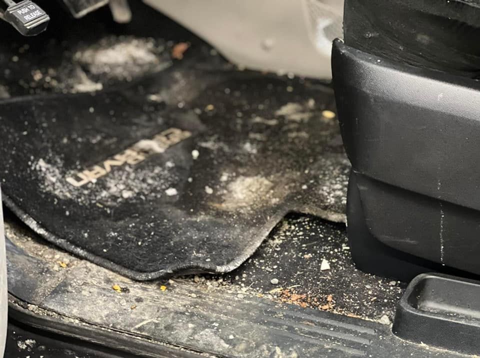 Dirty floor mat in a vehicle with scattered debris next to a black seat.