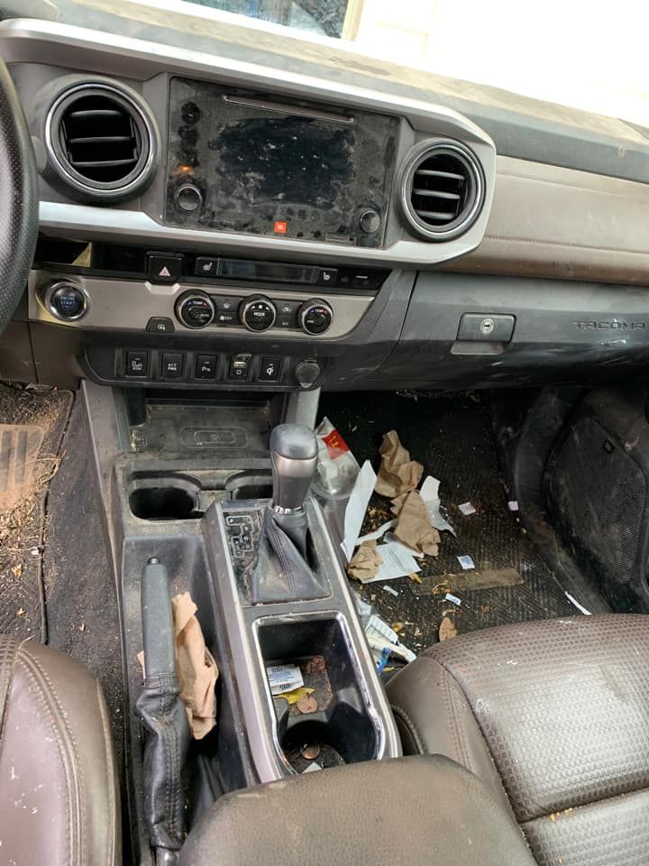 Interior of a dirty car with trash on the floor and dashboard. Dark brown leather seats and console.