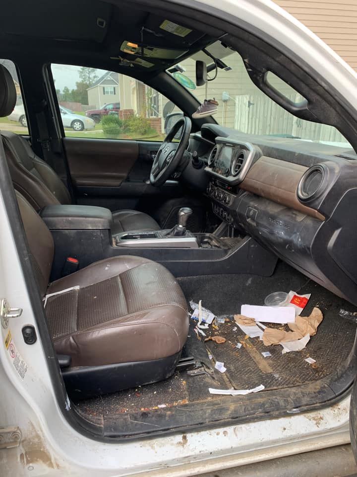 Dirty interior of a white Toyota Tacoma truck. Brown leather seats are visible, with debris on the floor.