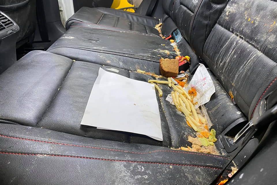Dirty car back seat covered in food and trash.
