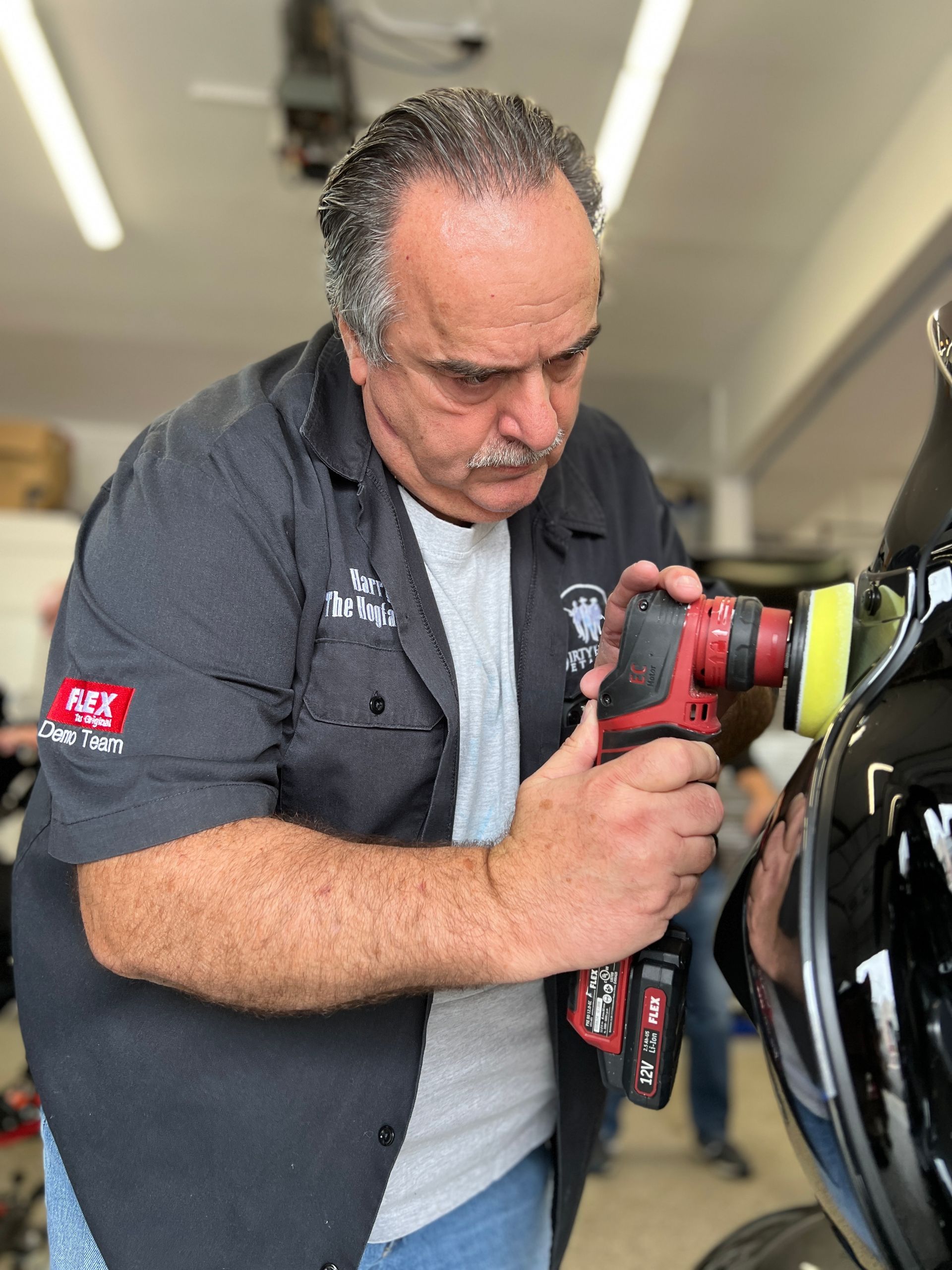 Man polishing black motorcycle fairing with a power tool in a garage.