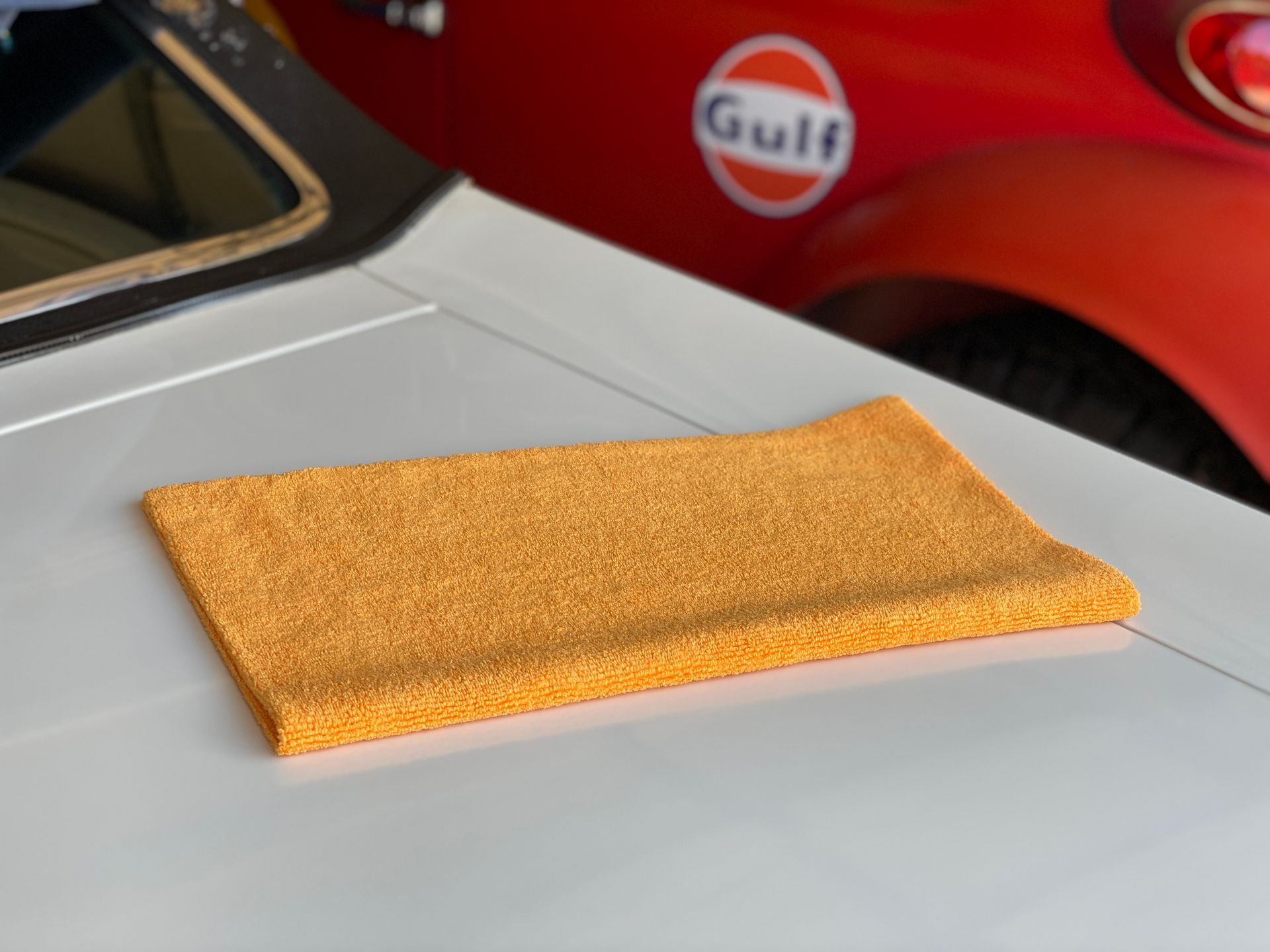 Orange microfiber cleaning cloth on a white car hood; red car with