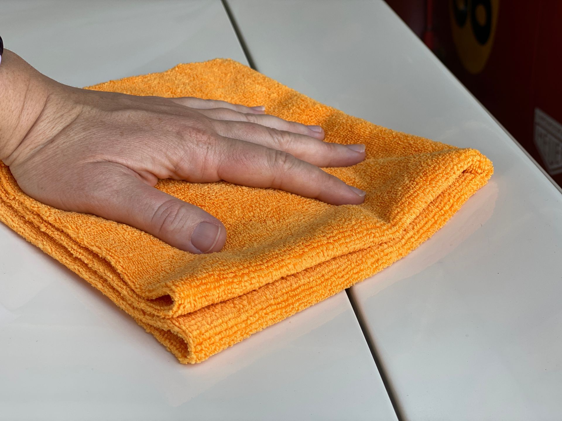 Hand on an orange microfiber cloth, cleaning a white surface.