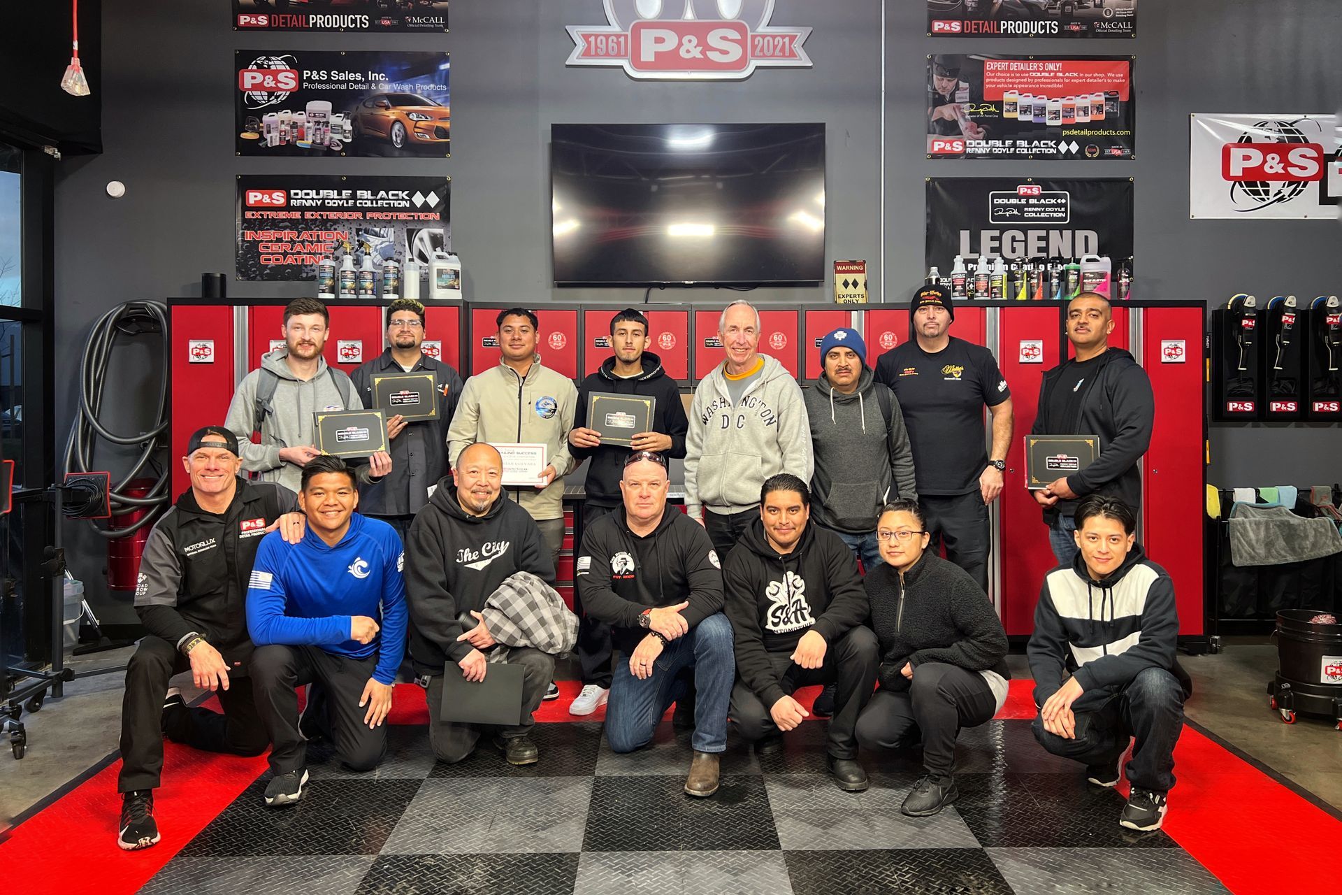 Group photo: a team of men and women pose indoors, holding items. Red storage lockers in the background.
