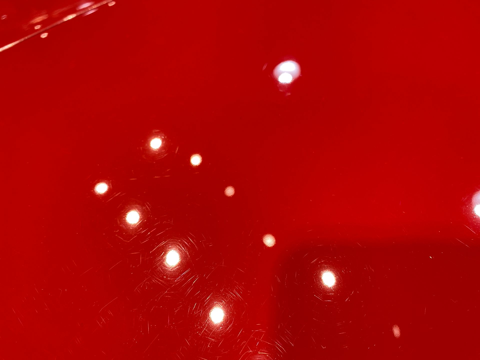 Close-up of red car paint showing swirl marks under bright lights.
