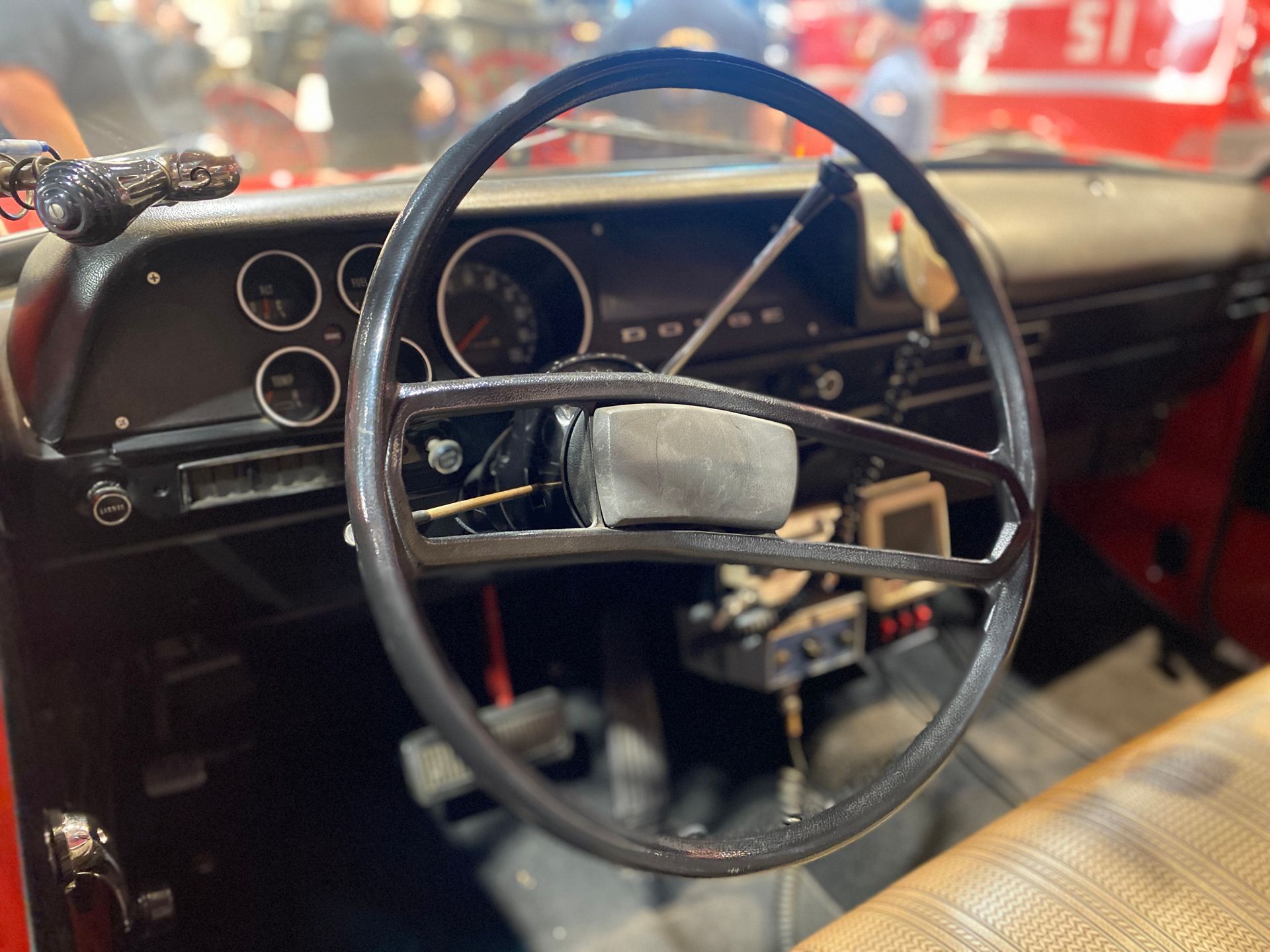 Close-up of a vintage vehicle's black steering wheel and dashboard with gauges; red interior.