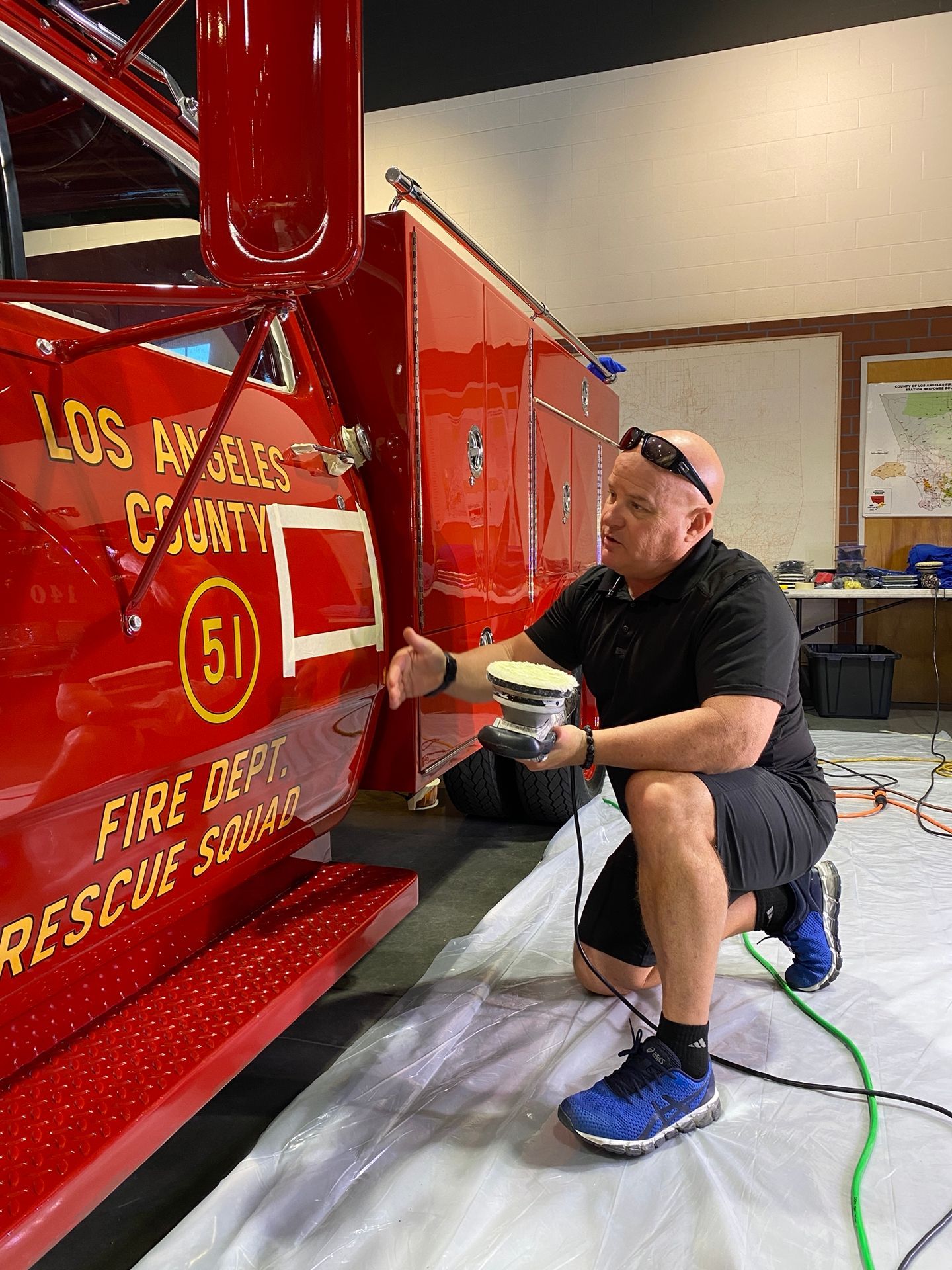 Firefighter polishing a red Los Angeles County fire truck in a garage.