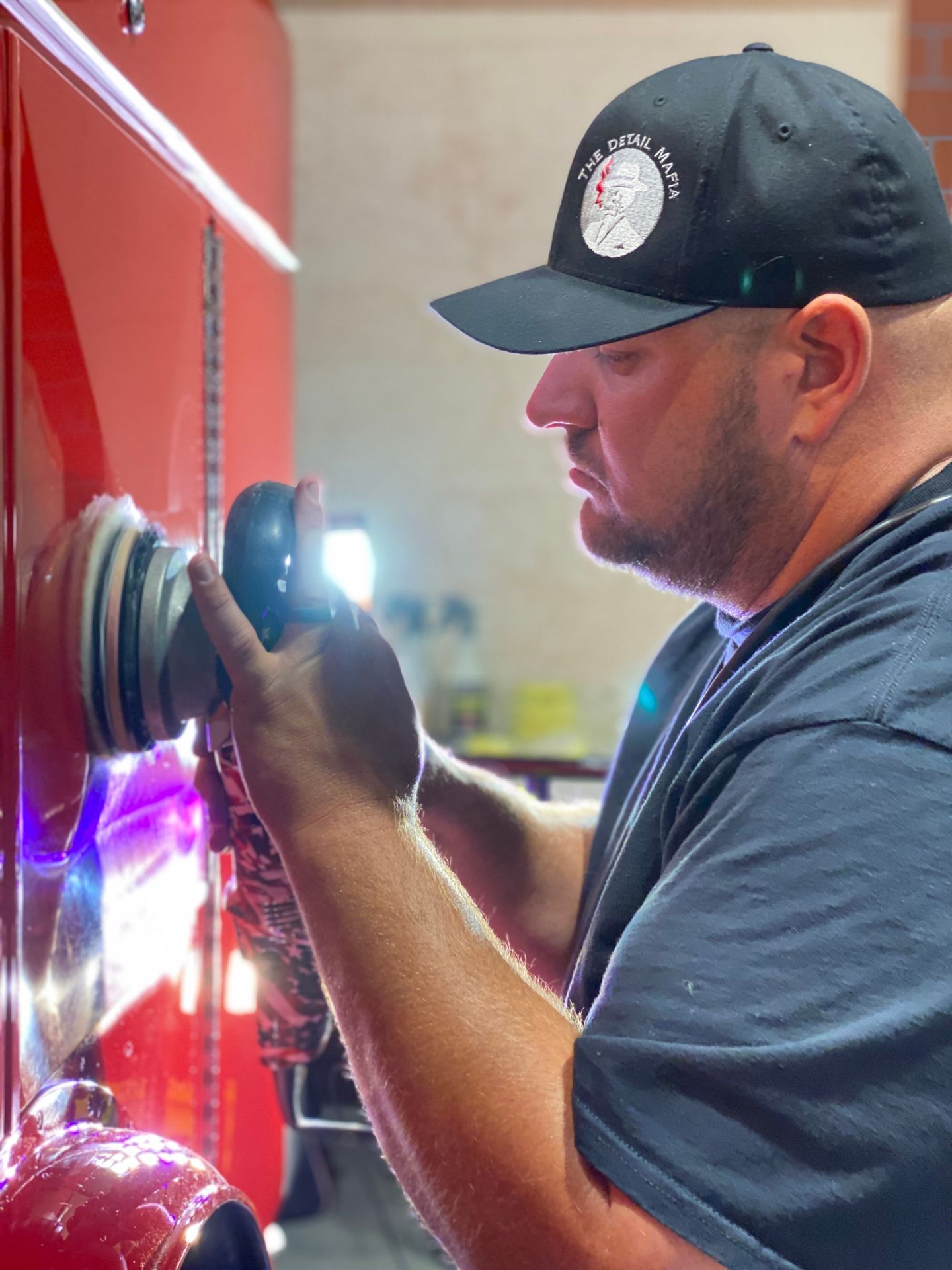 Man in a black hat polishing red fire truck with a buffing machine.