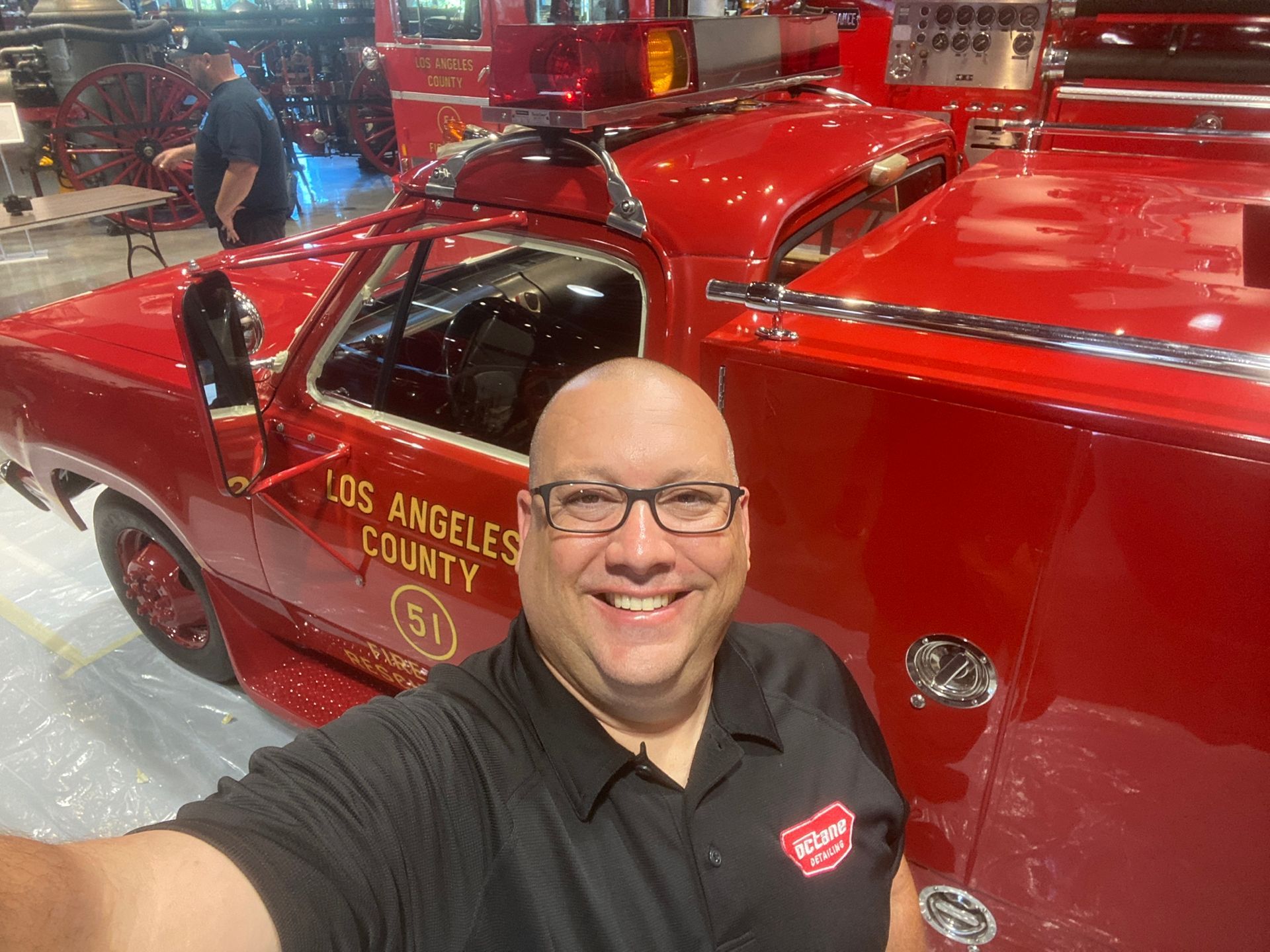 Man in glasses smiles beside a red Los Angeles County fire truck.