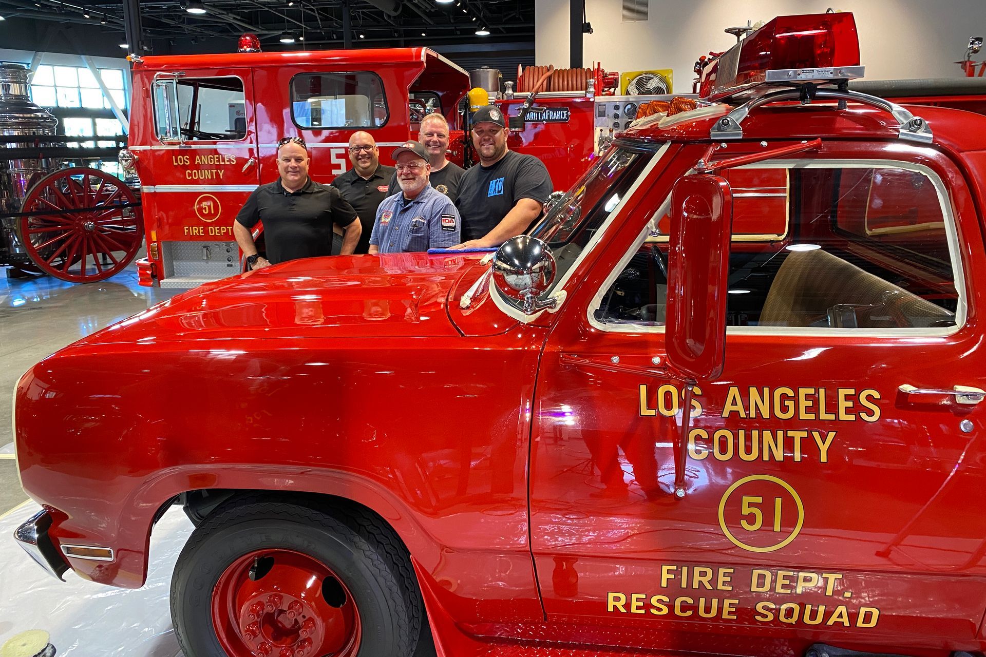 People pose with a red vintage Los Angeles County fire truck at a show.