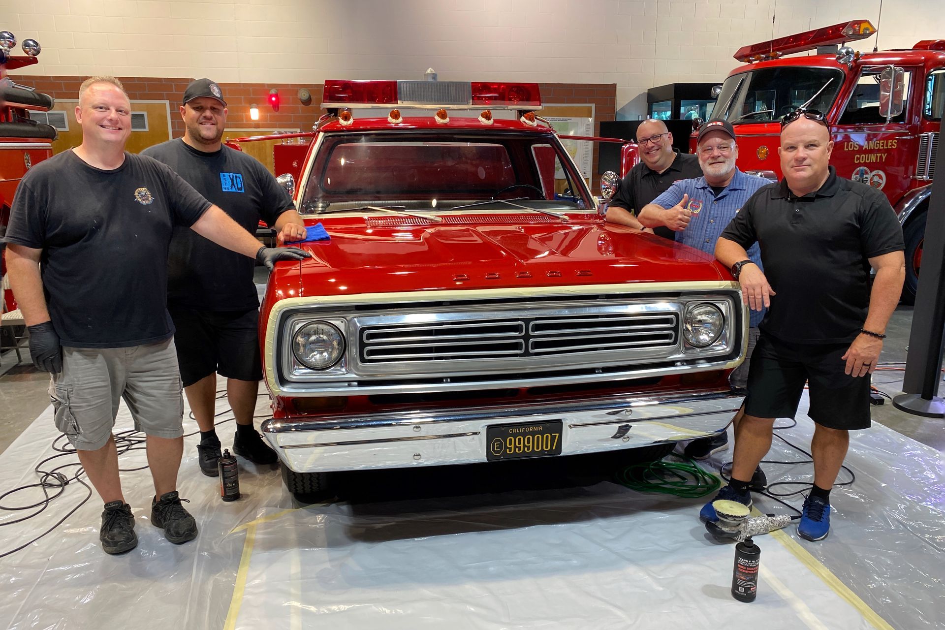 Group of men posing with a restored red truck. Indoor setting.
