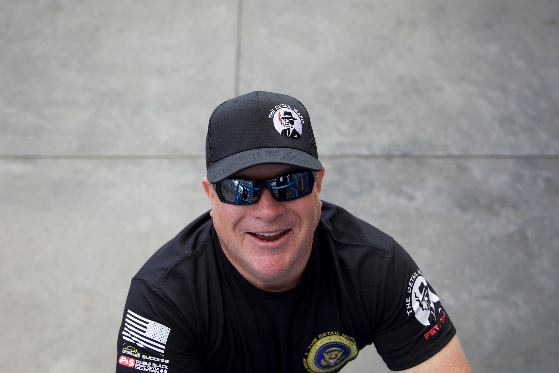 Man wearing sunglasses and a black cap, smiling, and looking at the camera.