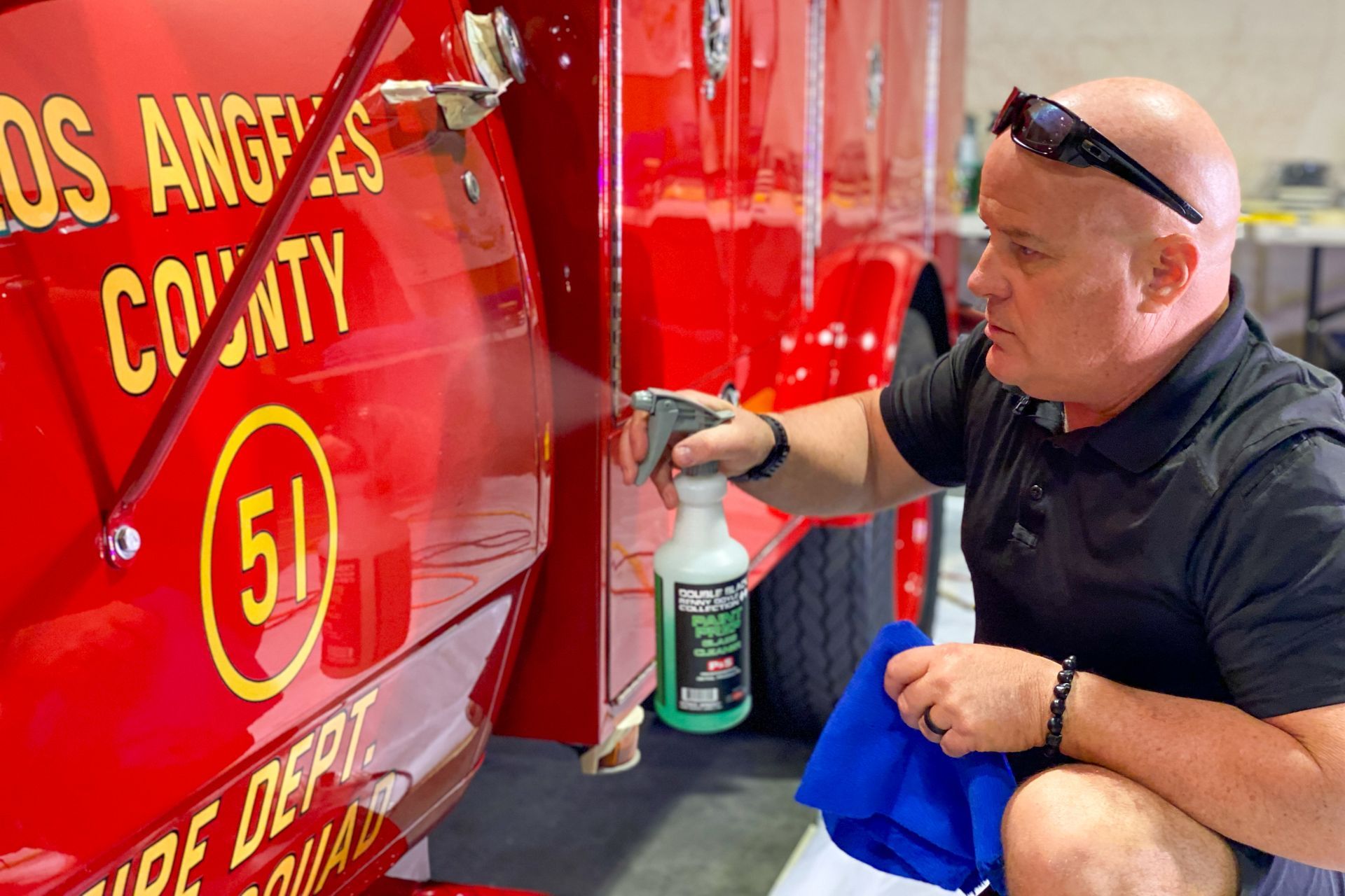 Man sprays and wipes the side of a red fire truck. It is labeled 