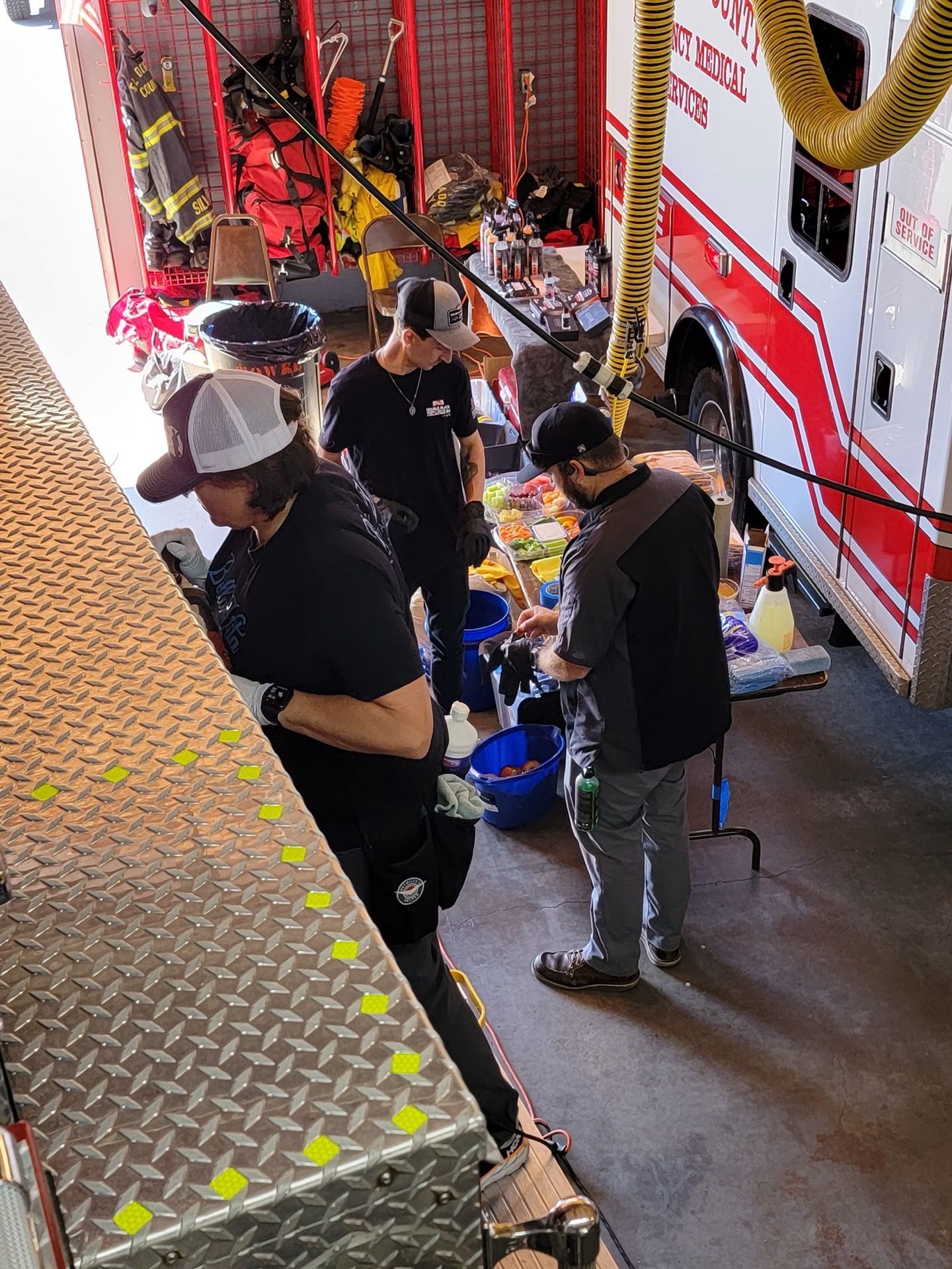 Firefighters preparing equipment in a fire station; three people near a red and white ambulance.