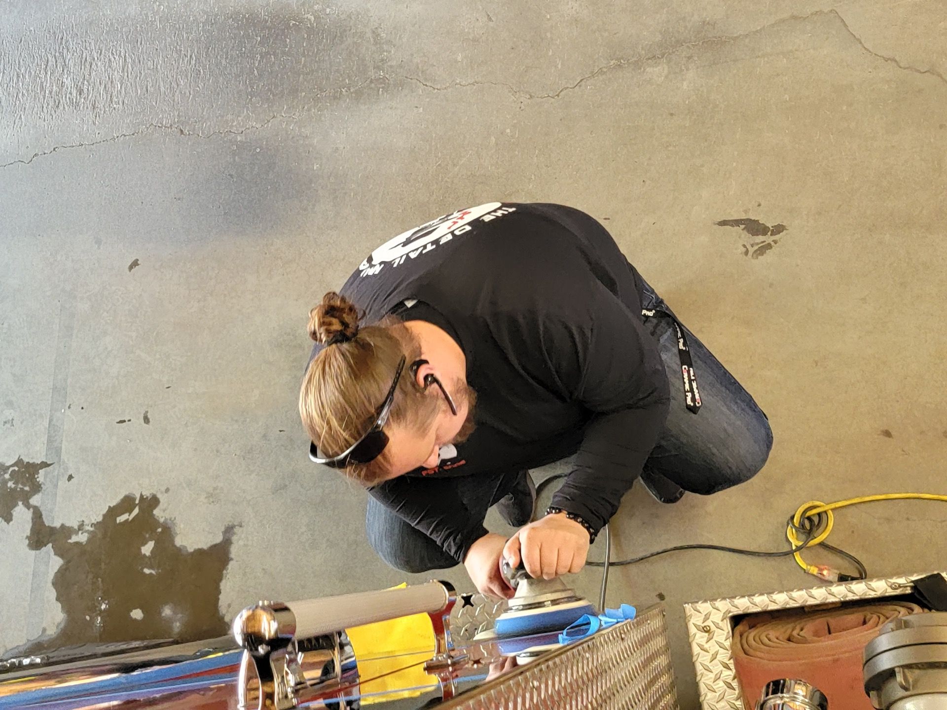 Man sanding metal with an electric sander, wearing sunglasses and working outside.