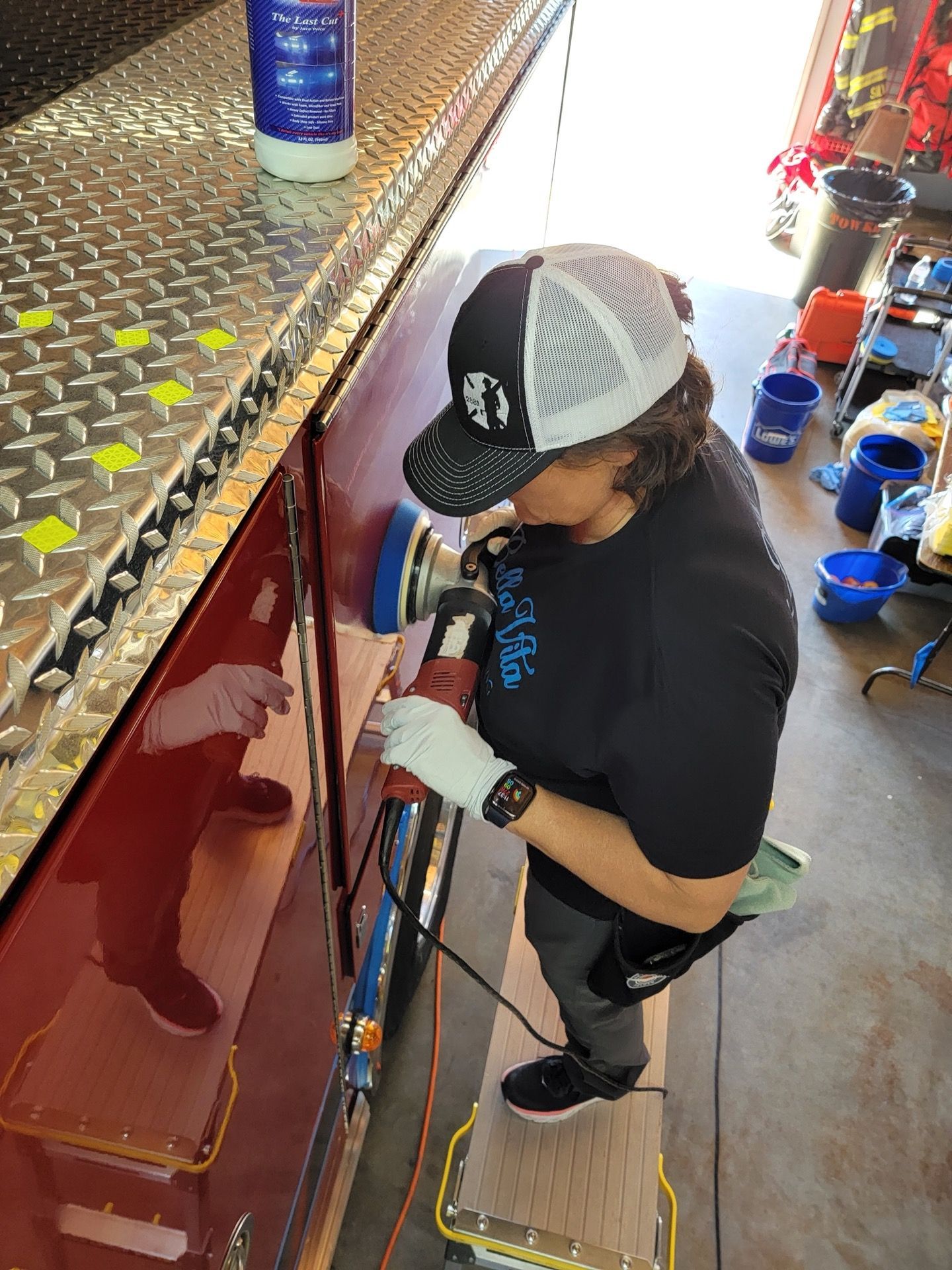 Woman polishing a red vehicle with a power tool; outdoors.