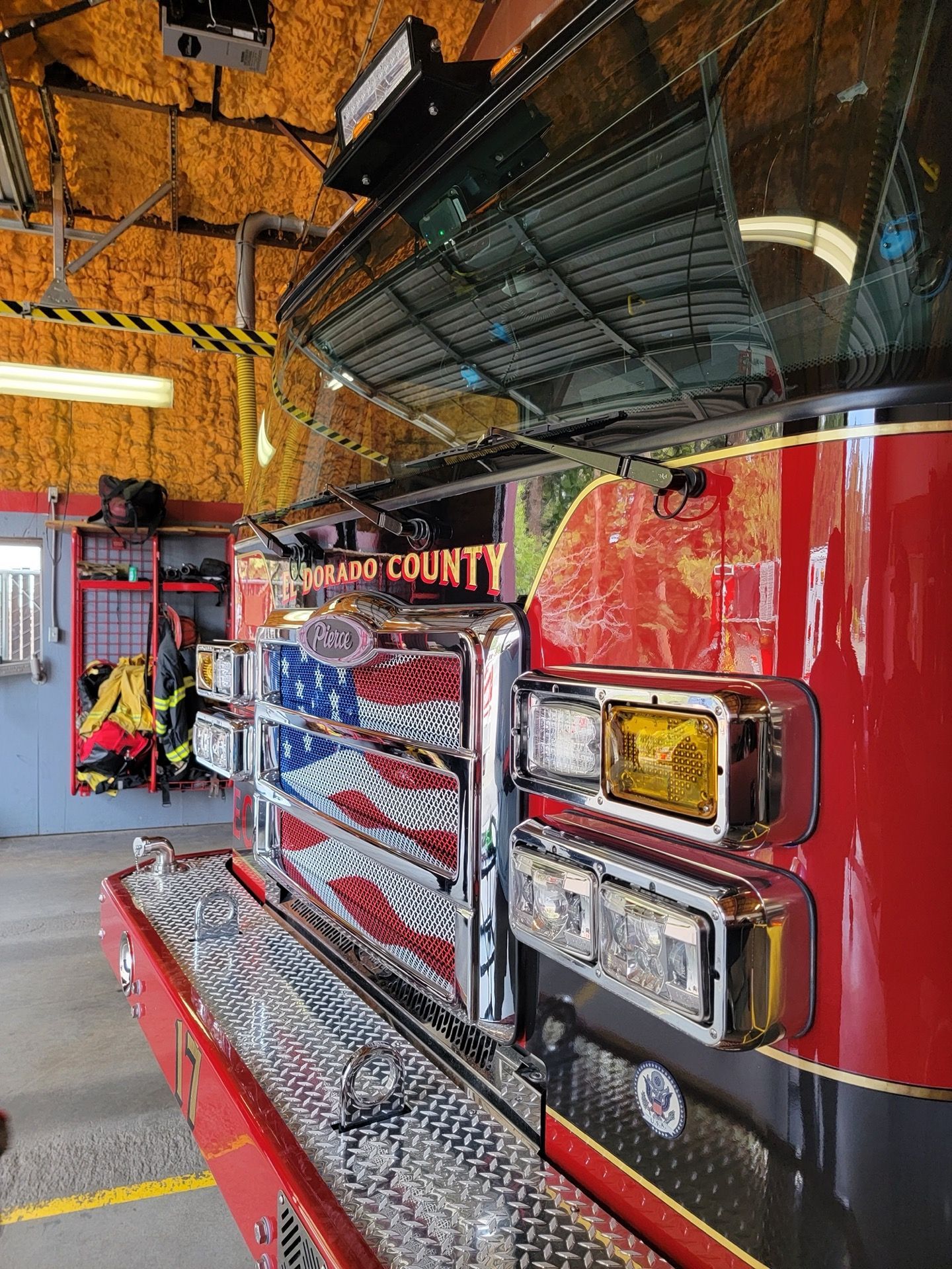 Fire truck, front view with American flag grille, parked inside a fire station. Reflective red paint.