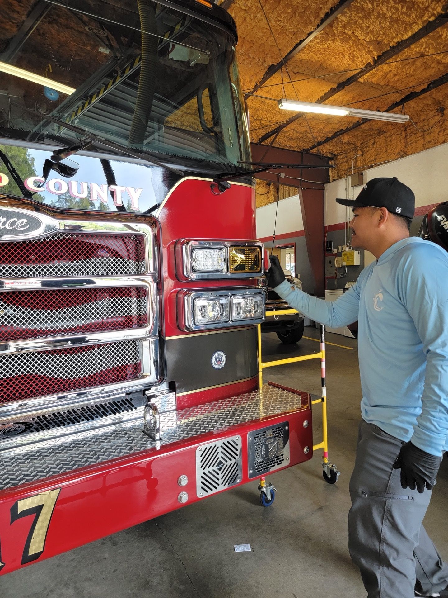 Man points to a fire truck's lights, in a red and metal garage. Fire truck says