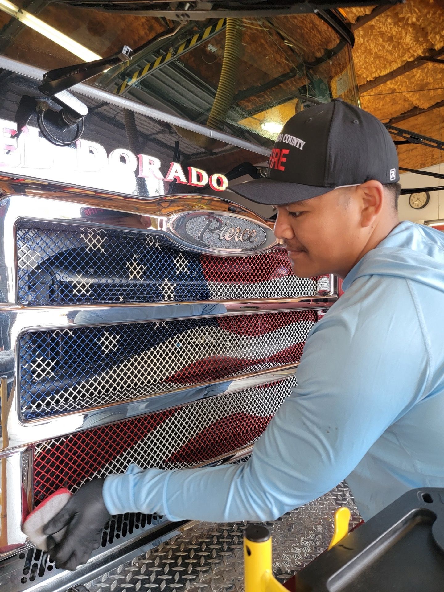 Man cleaning a vehicle grill with an American flag design. He's wearing a hat and light blue shirt.