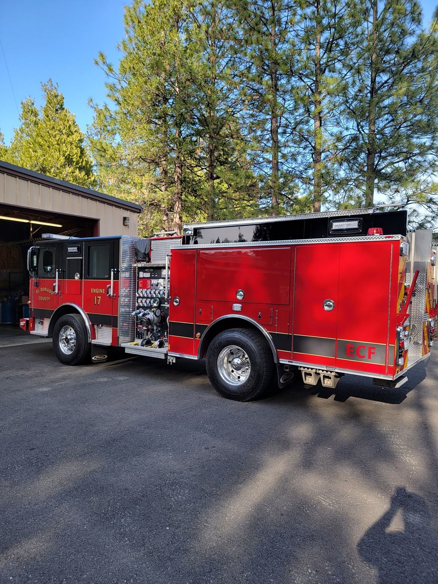 Red fire engine parked in front of a garage with trees in the background.