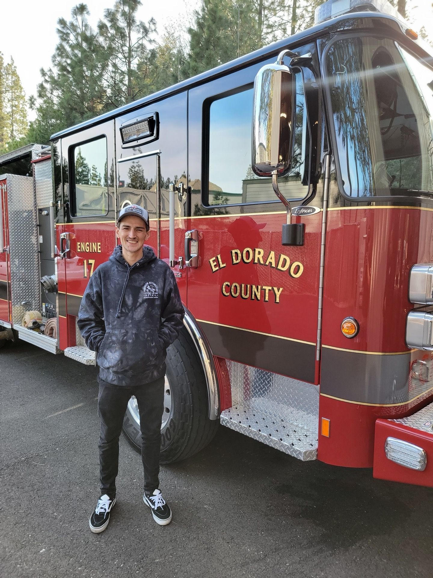 Man standing in front of a red and black El Dorado County fire truck, smiling.