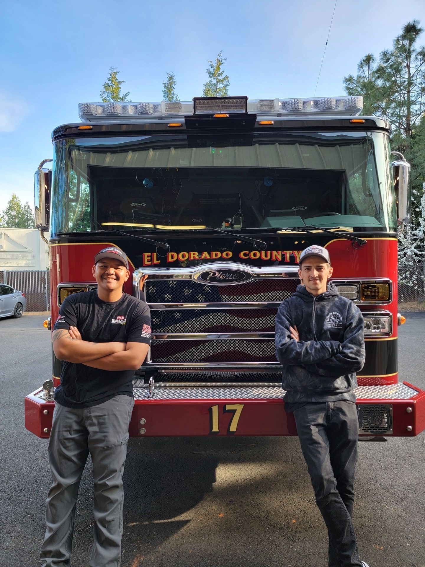Two firefighters stand in front of El Dorado County fire truck 17. Arms crossed, smiles.