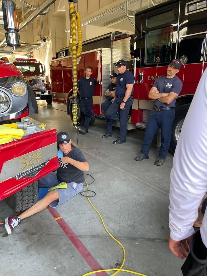 Firefighters at station; one works on truck, others observe.