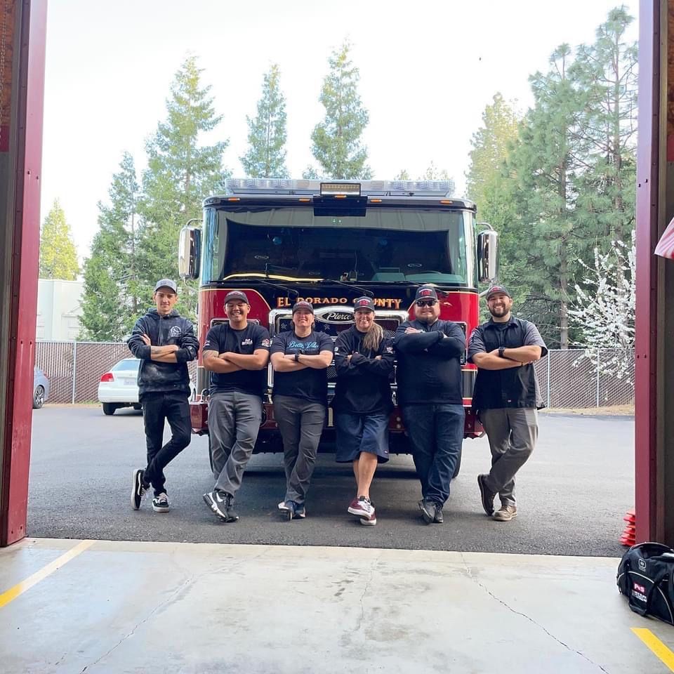 Firefighters posing in front of a fire truck, outdoors.