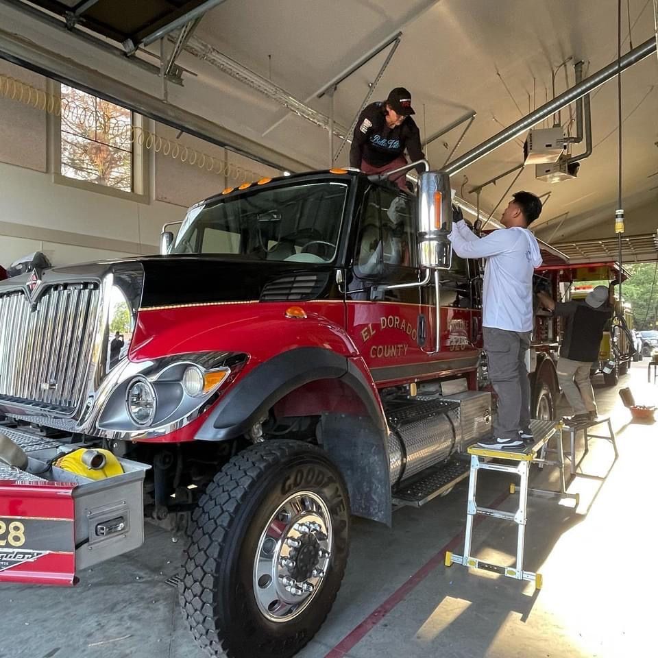 Firefighters working on a red and black fire truck in a garage.