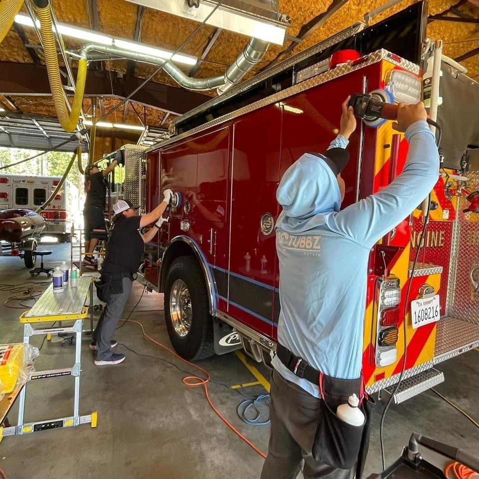 Two people working on a red fire truck in a garage, using tools and cleaning.