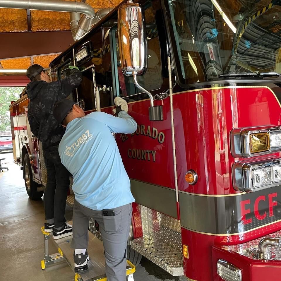 Two people working on a red fire truck, one on a step stool. Colorado County is visible.