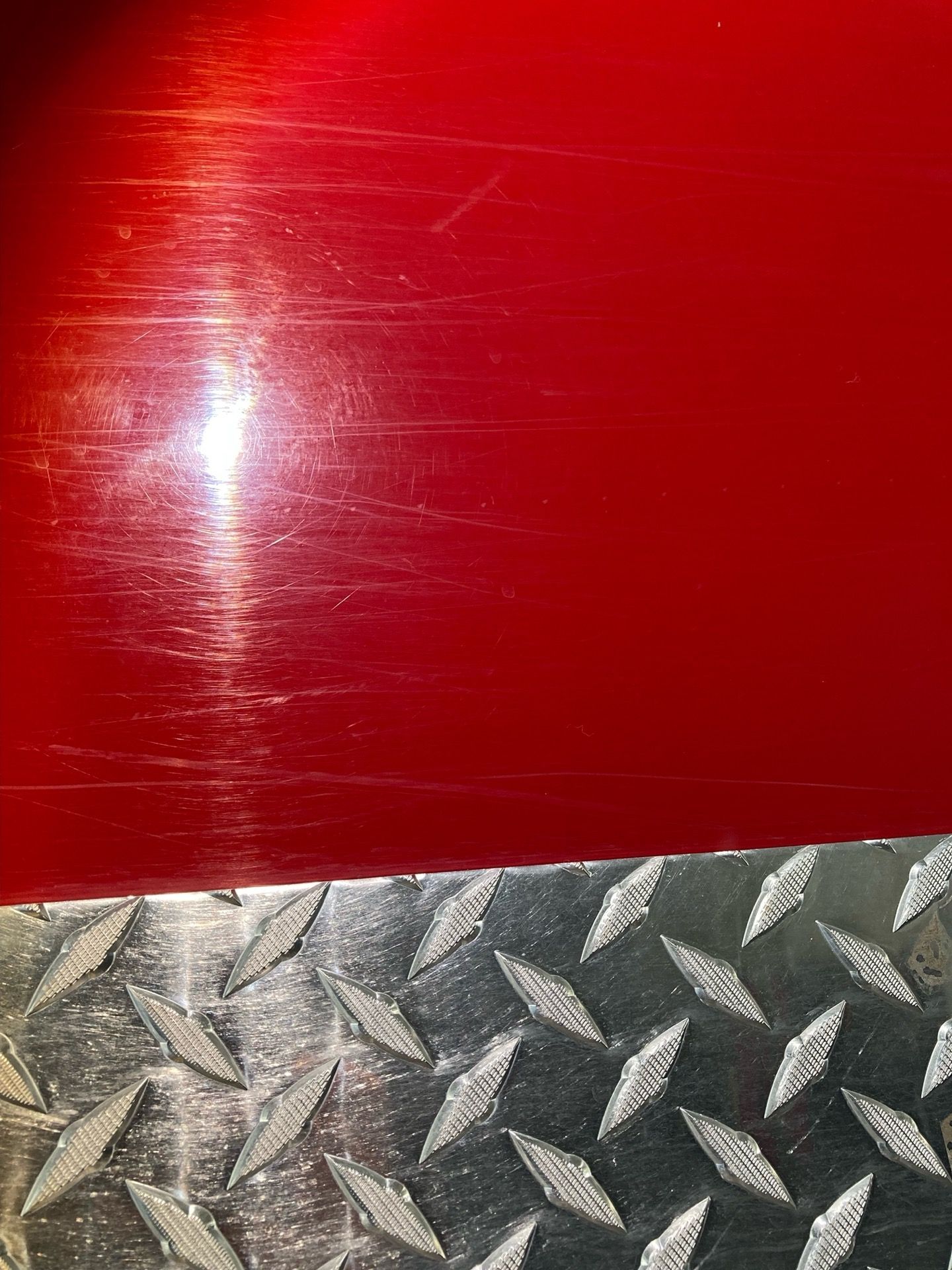 Red surface with scratches above a diamond plate metal surface.