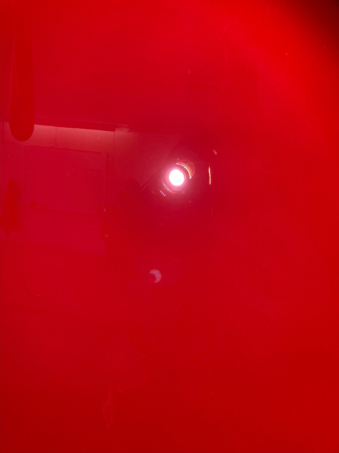 Bright white light reflecting off a red surface, with a dark spot near the bottom.