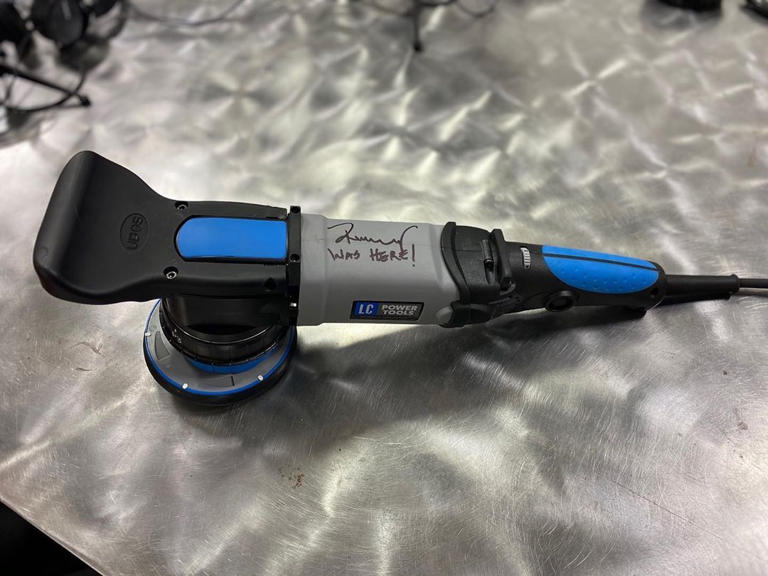 Blue and black electric polisher on a metal surface, with handwritten text on the side.