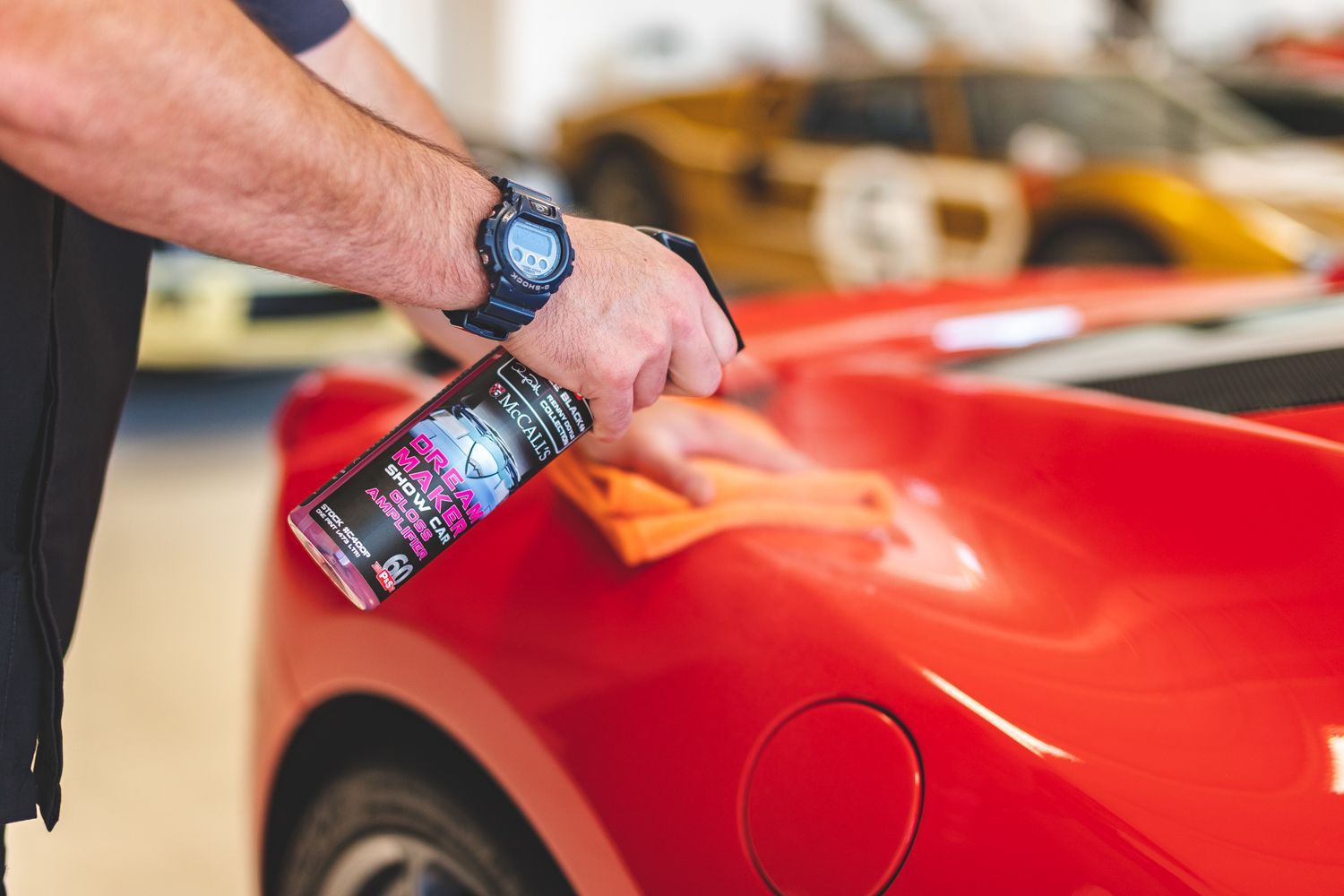 Man spraying red car with cleaning product in a garage, detailing a classic vehicle.