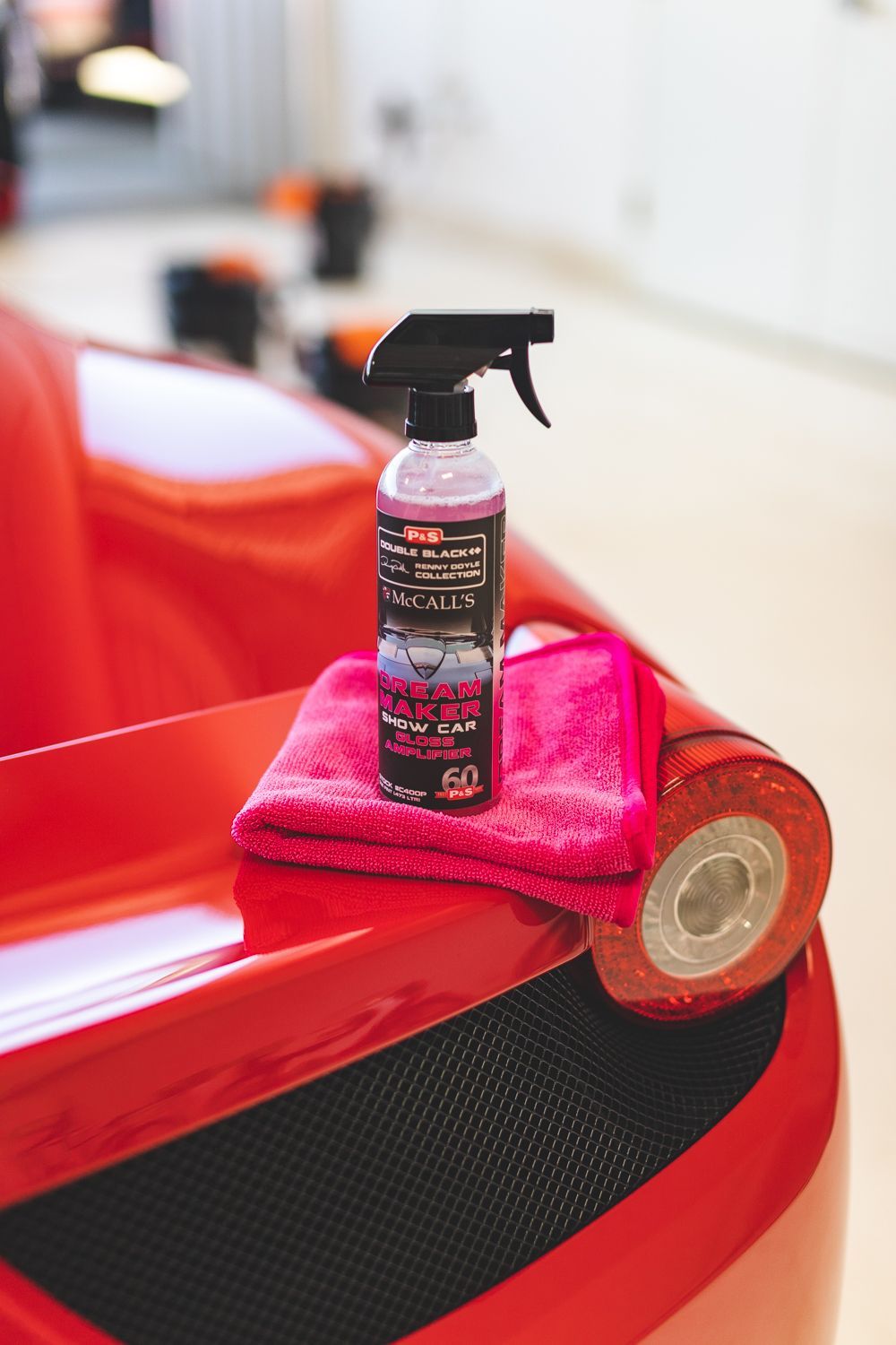 Spray bottle, pink microfiber towel, and detailing tape on a red car.