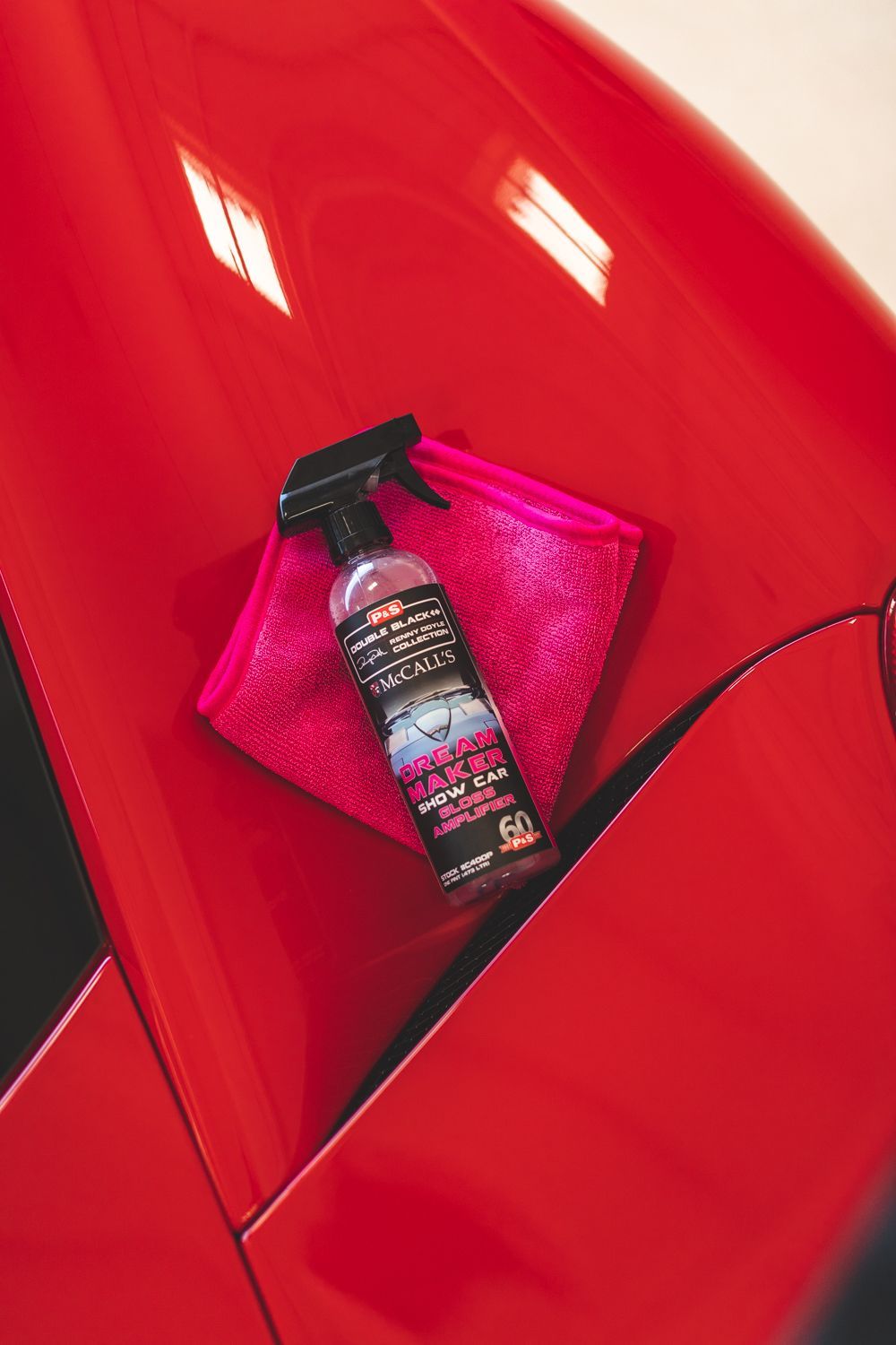Red car hood with a cleaning spray bottle and a pink microfiber cloth.