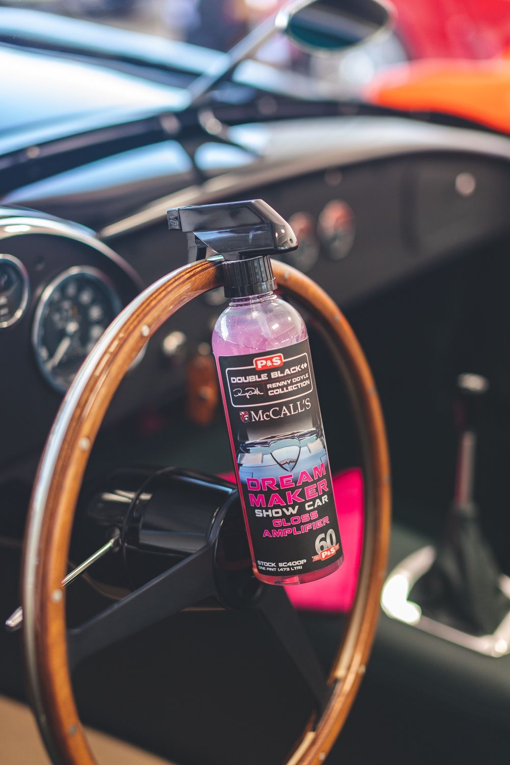 Spray bottle on a wooden steering wheel of a classic car. Interior shot; black, pink, and gray colors.