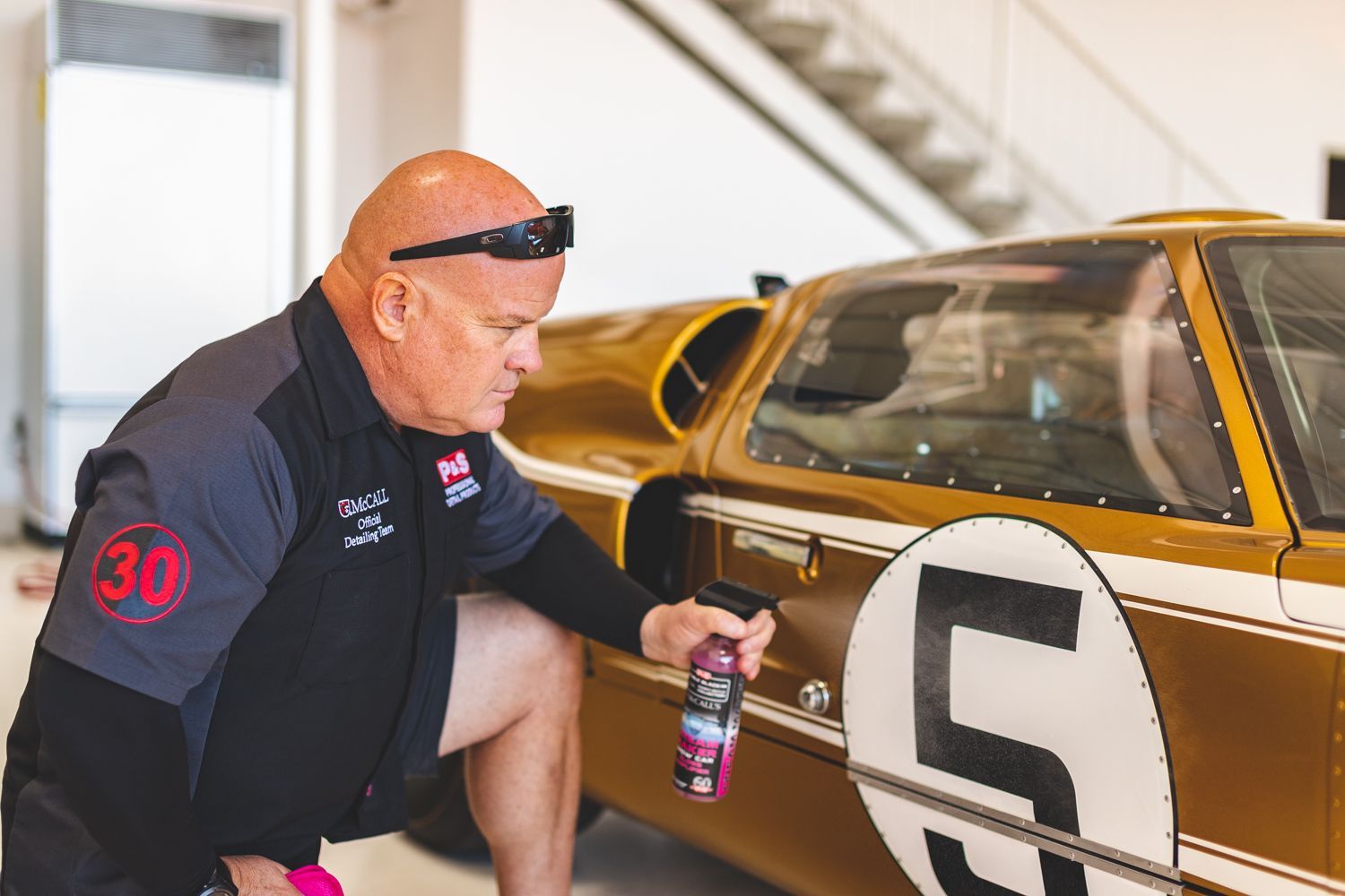 Man kneeling, spraying gold race car with number 